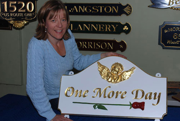 sandra freeman holding a custom gold leaf sign that says one more day with carved cherub and carved rose