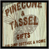 A hand painted background and vinyl lettering give the Pine Cone and Tassle sign a very unique look.